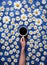 Hello summer. A cup of coffee in a woman`s hand on a blue background with chamomile or daisies. The concept of the
