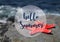 Hello Summer vacation message sign with starfish on the beach by the ocean.