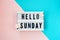 Hello Sunday - text on a display lightbox with flowers carnations on blue and pink background