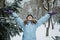 Hello winter, happy wintertime. Happy young curly woman with hands raised up celebrating winter snow standing in snowy