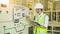 A helmeted technician holds a clipboard while checking and taking notes on the electrical control cabinet