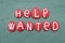 Help Wanted text composed with red colored stone letters over green sand