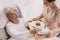 Helpful volunteer in beige uniform serving coffee to senior female patient