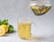 Herbal tea with ginger and mint is poured into a glass from a teapot on a light background with fresh lemon. The concept of a