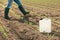 Herbicide jug container in corn seedling field, farmer walking in background