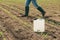 Herbicide jug container in corn seedling field, farmer walking in background