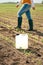Herbicide jug container in corn seedling field, farmer walking in background