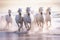 Herd of white horses trotting along a beach