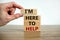 Here to help symbol. Male hand builds stack from blocks with words `i am here to help`. Wooden table. Beautiful white background