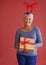 Heres a little something for you. Shot of a mature woman holding a gift and wearing festive reindeer antlers.