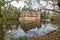 Het Oude Loo castle with its moat with reflection in the water and its bridge seen through the branches of a tree with green leave