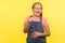 Hey you! Portrait of glad little girl with braid in denim overalls pointing finger to camera and laughing loudly