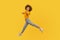 Hey you! Portrait of lively energetic curly-haired girl in urban style outfit walking through air in wide strides