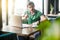 Hey you! Young serious businessman in green t-shirt sitting and working on laptop, looking at camera with warning sign