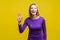 Hi! Portrait of sweet happy woman with raised hand saying hello to camera. indoor studio shot isolated on yellow background