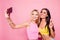 Hi there! Two beutiful pretty cheerful smiling attractive charming girlfriends dressed in colorful tops are making a selfie and d