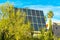 Hidden solar pannel with plants and palm trees with whispy blue sky background in late afternoon sun in urban area