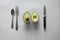 High angle shot of an Avocado, a knife and spoon and fork on a white surface