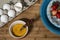 High angle shot of beaten eggs in a small bowl with and strawberries on a plate on the wooden table