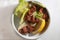 High angle shot of a bowl of meat, kale and a slice of lemon on a white surface