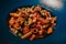 High angle shot of a bowl of penne pasta with meat, olives, sauce, and chili pepper on a table