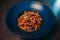 High angle shot of a bowl of penne pasta with meat, olives, sauce, and chili pepper on a table