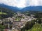 High angle shot of a city with houses and churches surrounded by a forest and cloudy mountains