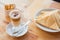 High angle shot of a cup of Caffe macchiato next to pastries and sugar packets on a wooden surface