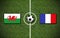 High angle shot of the flags of France and Wales with a soccer ball in the center on a soccer field