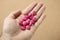 High angle shot of a human\'s hand with a handful of pink pills, on a pink background