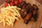 High angle shot of saucy chicken wings, french fries, and tomatoes on a kitchen board