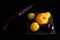 High angle shot of some peaches and plums and a knife on a black surface