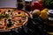 High angle shot of testy pizza along with vegetables and charcoal on wooden surface