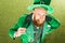 High angle view of bearded man in green costume holding clover shaped eyeglasses and looking at camera
