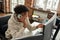 High angle view of busy young male stock trader talking on the phone with client while using computer, sitting at desk