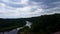 High angle view of calm flowing river surrounded by lush green forests under cloudy overcast sky with candid hiker walking