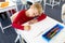 High angle view of caucasian elementary schoolboy writing on book at desk in school