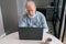 High-angle view of focused aged mature elderly male looking at laptop screen working on computer sitting at kitchen