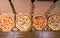 High angle view of four pizzas with variety of toppings and cheese in cardboard take out boxes