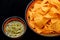 High angle view of homemade basil pesto sauce with nachos corn chips on black background with space for text