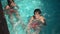 High angle view of proud confident little boy and girl sitting in bubbling water in swimming pool in sunbeam looking at