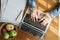 High-angle view shows a woman`s hands are typing on laptop . which has papers and fruits put on the table at the The sun shines