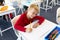 High angle view of smiling caucasian elementary schoolboy looking away while writing on book at desk