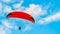 High in blue cloudy summer sky, tandem of paragliders is flying on red paraglider.