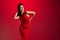 High fashion model wearing tight midi red dress and posing over gradient red-burgundy studio background in neon light.