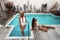 High fashion two bikini models with sexy body in white swimwear posing by swimming pool at luxurious villa. Glamour Portrait of