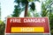 High fire danger sign informs the public that wildfires are likely. Green forest background