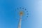 High flying carousel against strait blue sky and airplane line at summertime on a large pole and 16 colored stools in blue red