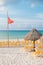 High hazard or currents warning flag on an empty beach with yellow chairs and palm tree leaf umbrella on a sunny day