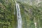 High large green waterfall in Milford Sound New Zealand